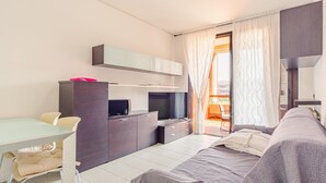 A modern, well-lit room with a sofa, a dining table, a TV, and a cabinet. - Fior di Loto - Italian Homing (Desenzano del Garda)