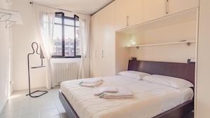 A neatly arranged hotel room with a bed, a radiator, a window with curtains, and a mirror above the bed. - Fior di Loto - Italian Homing (Desenzano del Garda)