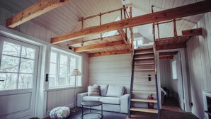 Een kamer met een houten plafond, een witte bank, een ronde tafel en een ladder.