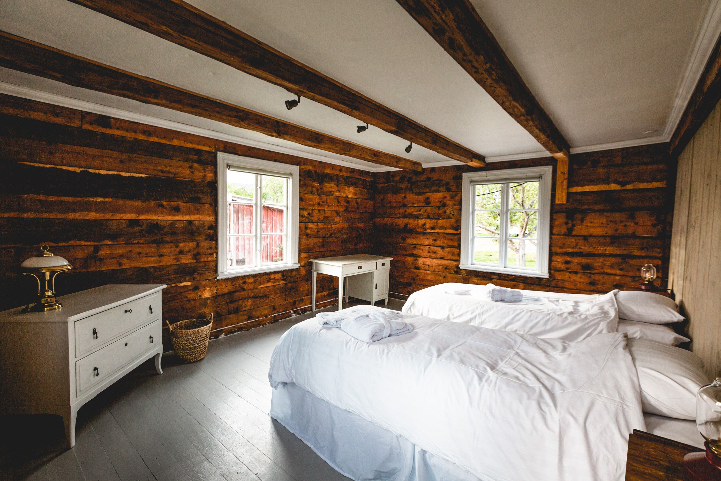 Een slaapkamer in een blokhut met een bed, een dressoir en twee ramen.