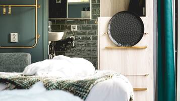 A modern bedroom with a bed, a dresser, a mirror, and a bathroom visible through an open door.