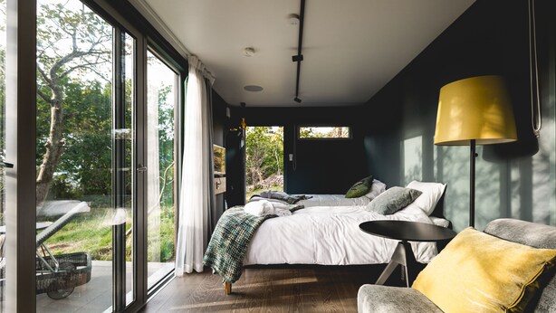Een slaapkamer met een groot bed, een nachtkastje, een stoel en een raam met uitzicht op groen.