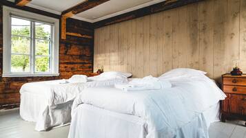 A room with two beds, wooden walls, a window, and a dresser.