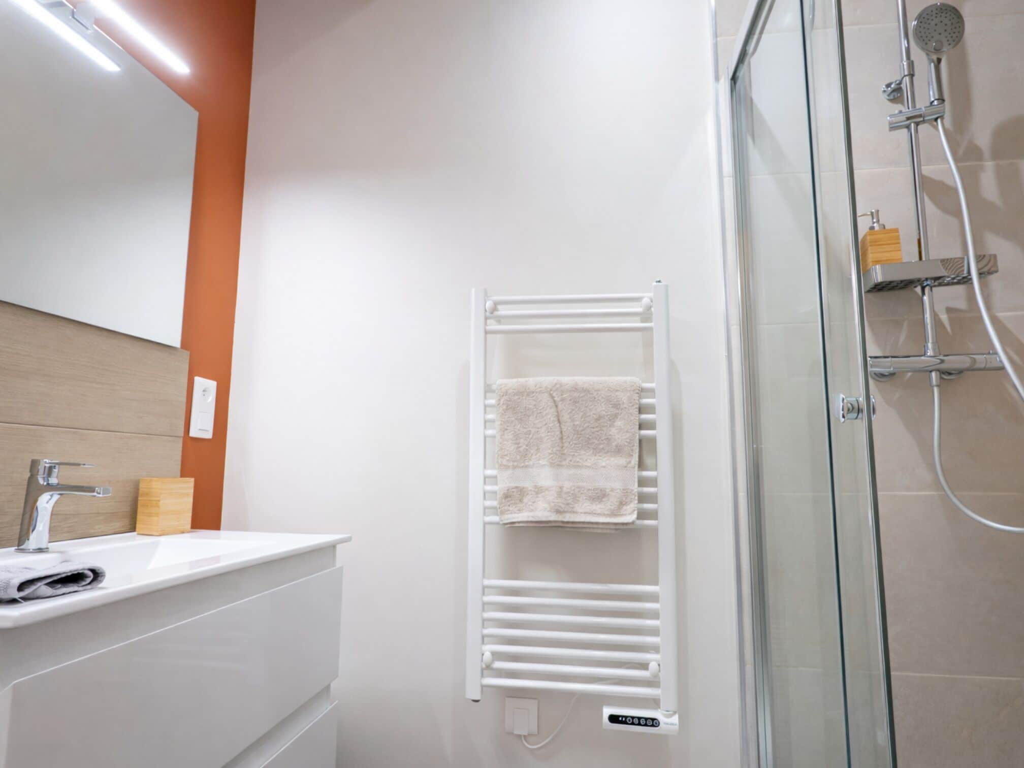 A modern bathroom with a glass shower enclosure, a white towel rack, and a wooden soap dispenser.