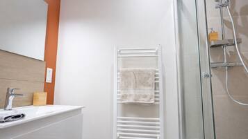 A modern bathroom with a glass shower enclosure, a white towel rack, and a wooden soap dispenser.