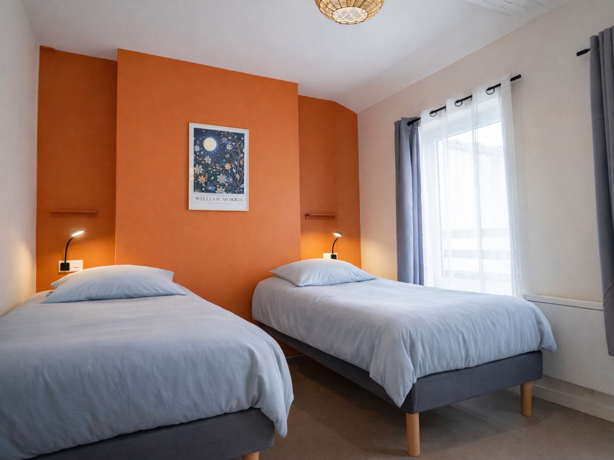 A room with two beds, a nightlight, a window with curtains, and a wall-mounted picture.