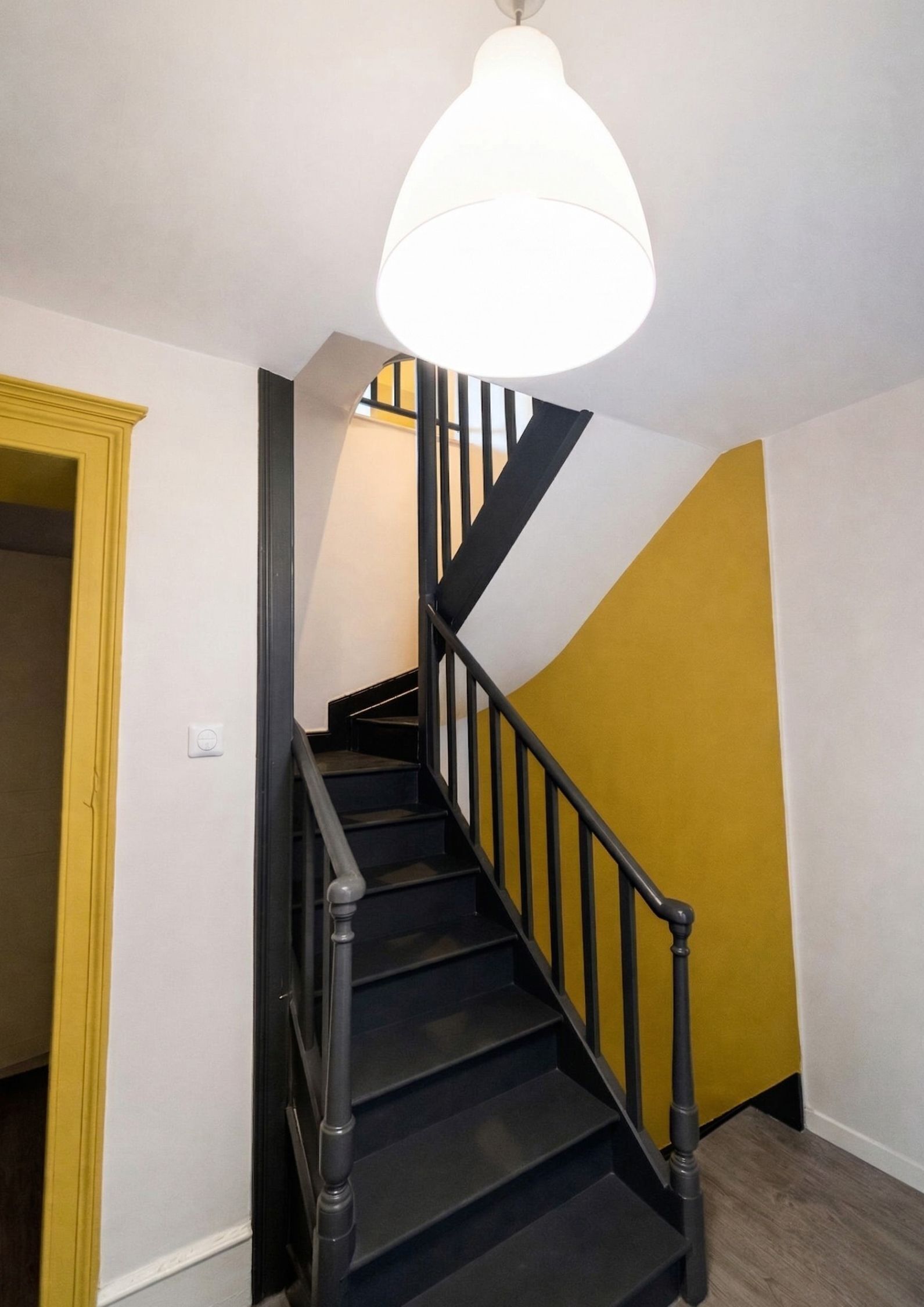 Una escalera con barandillas negras y una lámpara blanca.