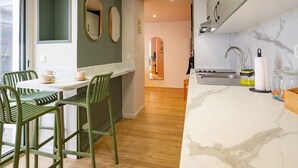 A modern kitchen with a marble countertop, green chairs, and a dining area with a window.