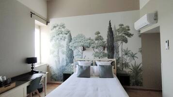A bedroom with a bed, a desk, and a chair. There is a window on the left side.