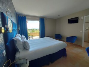 Habitación de hotel con una cama grande, un televisor montado en la pared y un balcón con cortinas azules.