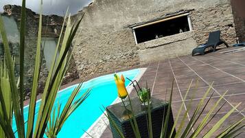 A swimming pool with stone walls and a window, surrounded by tropical plants.
