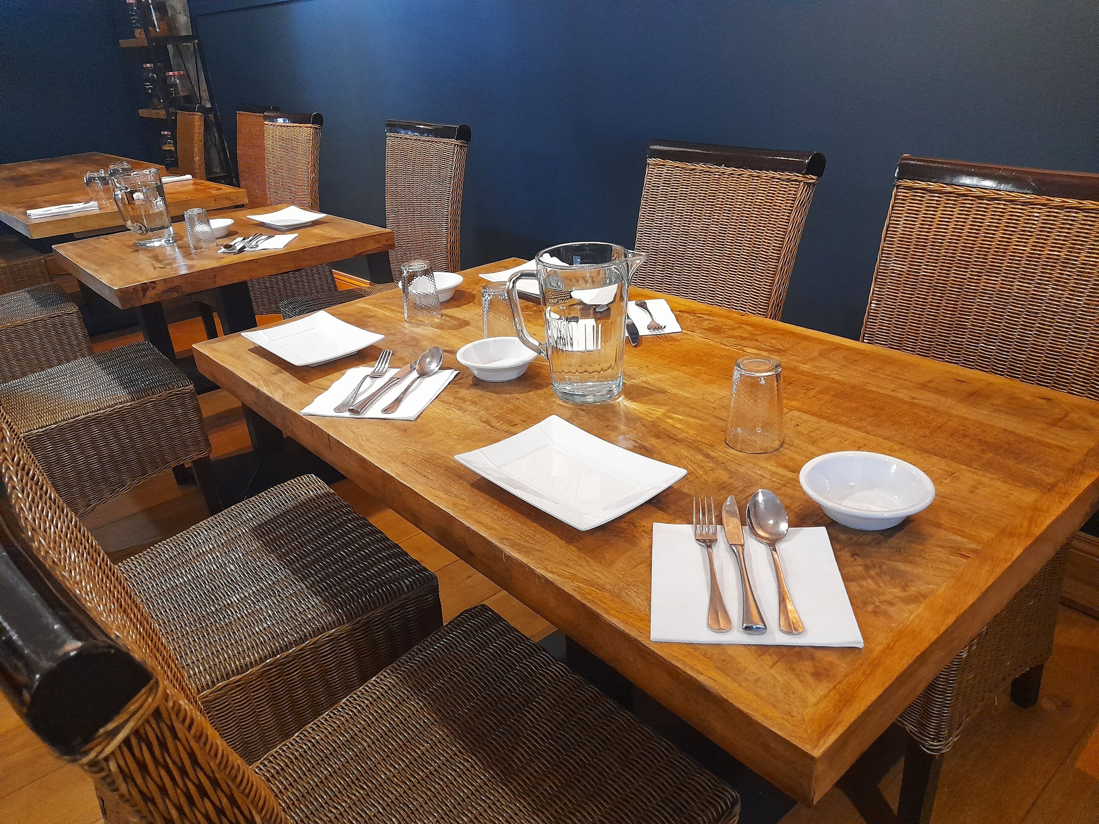 A dining area with wooden tables and wicker chairs, equipped with cutlery and glassware.
