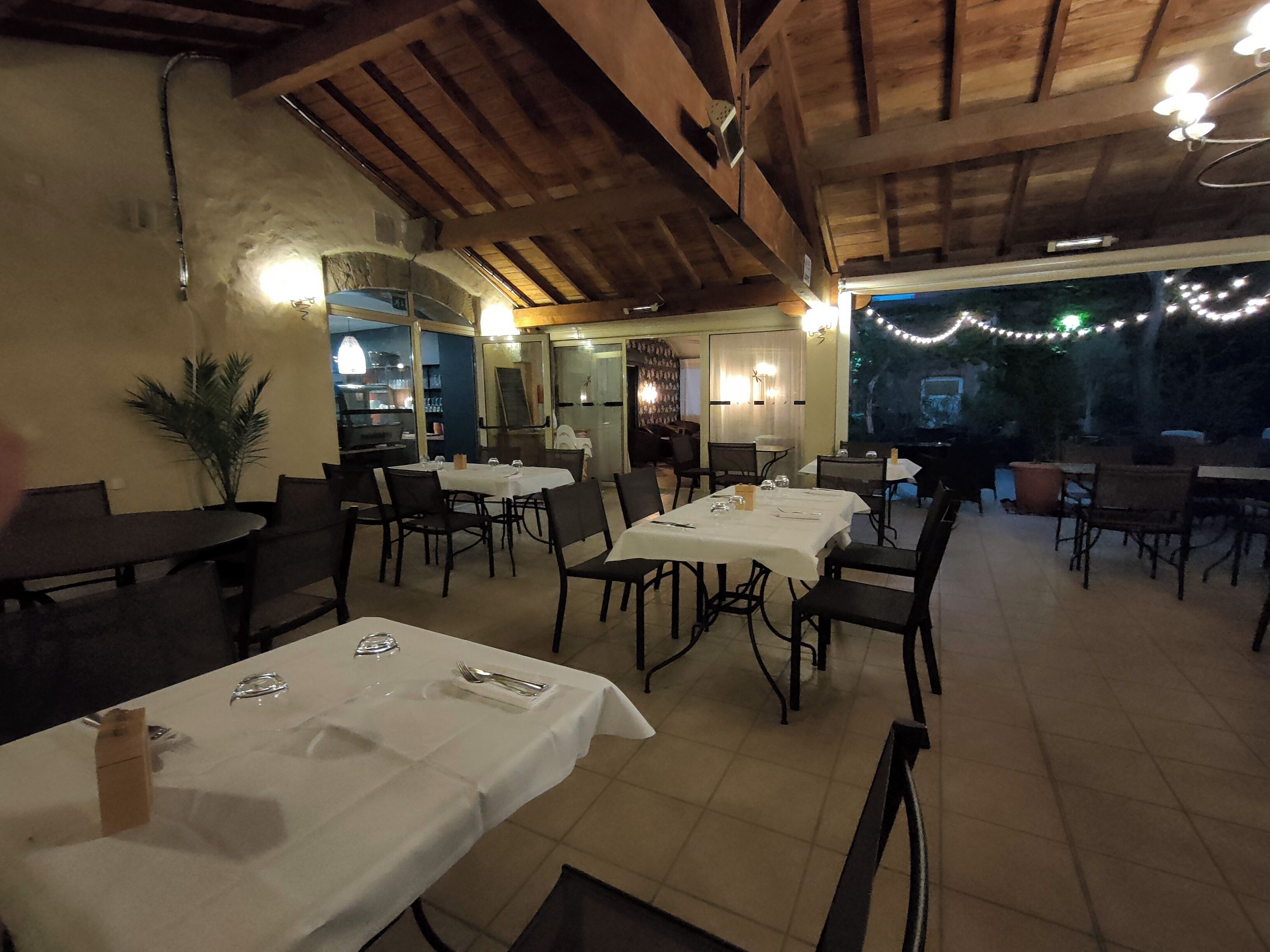 Un comedor interior con mesas preparadas para dos, vigas de madera en el techo y luces colgantes.