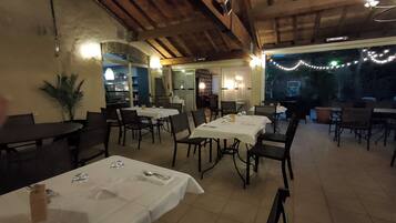 Un comedor interior con mesas preparadas para dos, vigas de madera en el techo y luces colgantes.