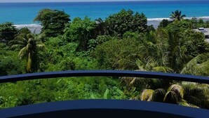 A view from a balcony overlooking a beach with dense greenery and a clear blue sky. - Beau Vallon Studios (Mahé Island)