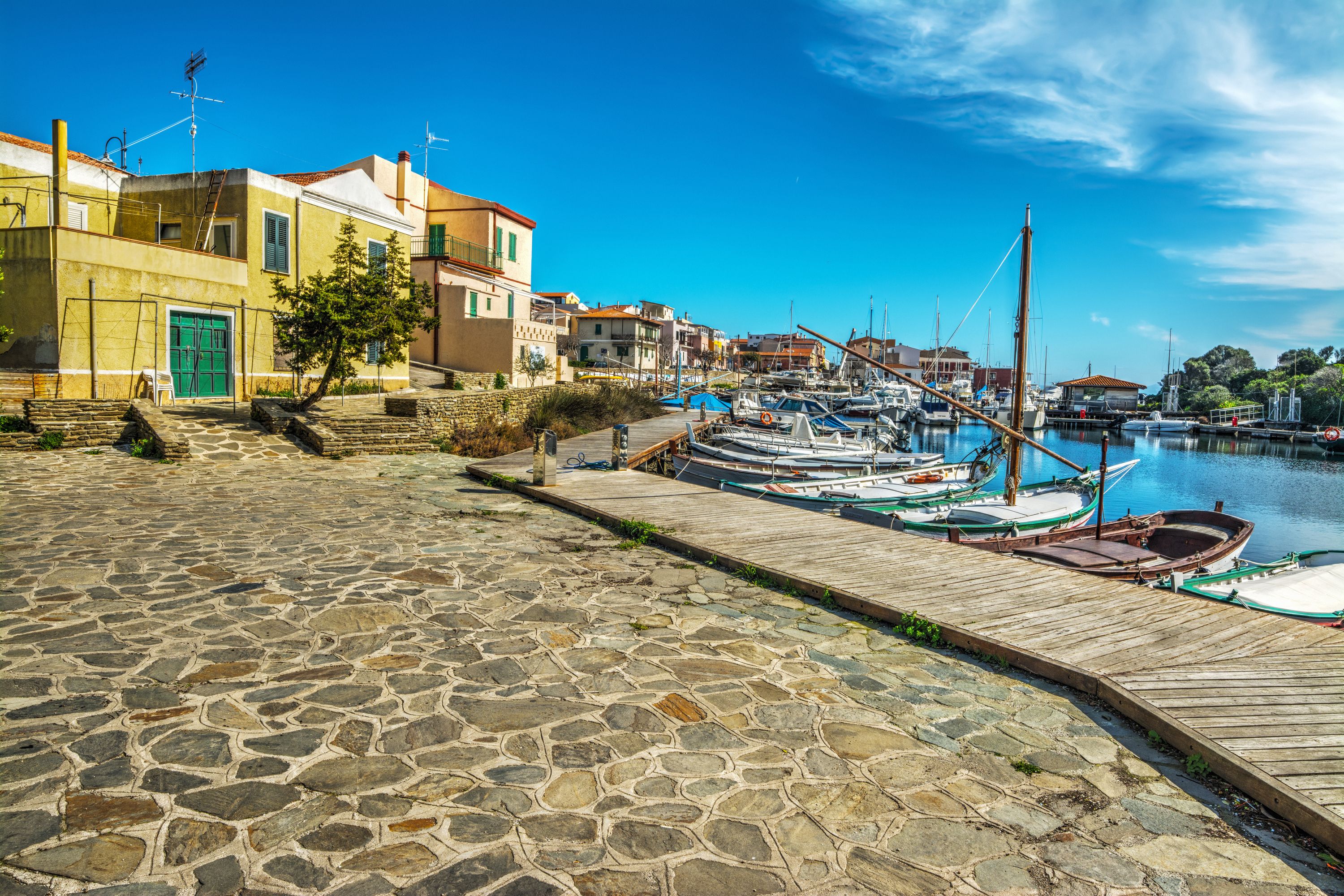 A stone-paved waterfront with boats docked and buildings along the shore.