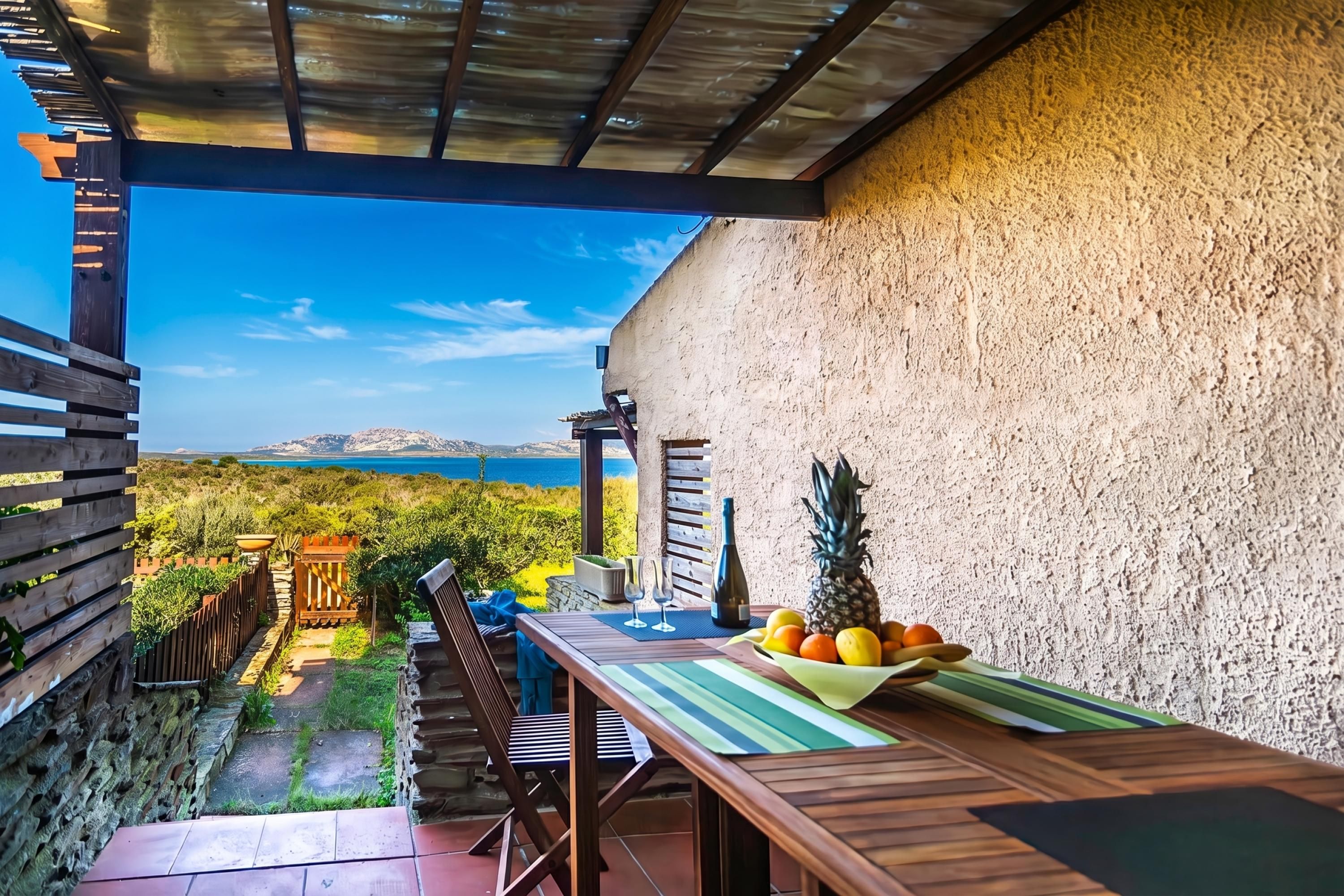 An outdoor patio with a table set for two, a bottle, and a bowl of fruit.