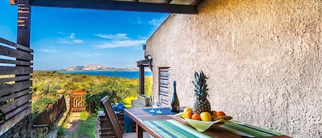 An outdoor patio with a table set for two, a bottle, and a bowl of fruit.