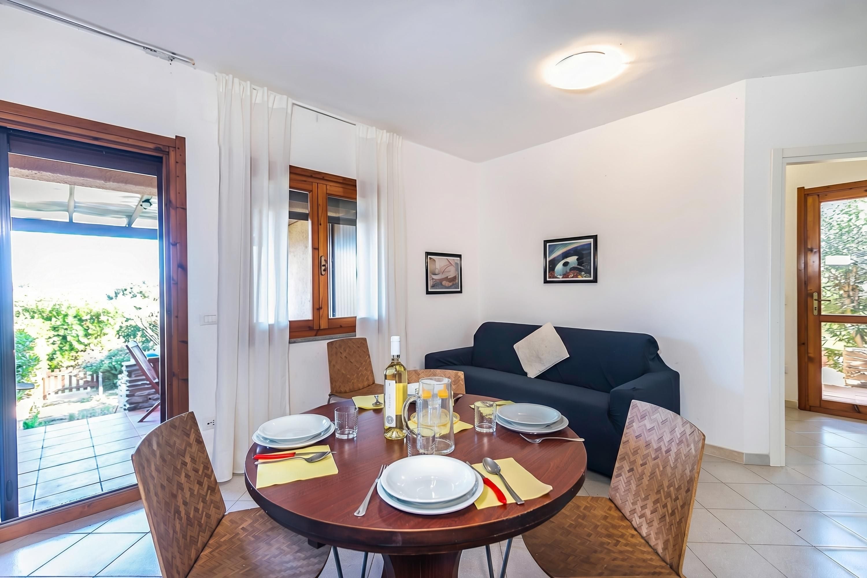 A dining area with a round table set for four, a sofa, and a view of the outdoors.