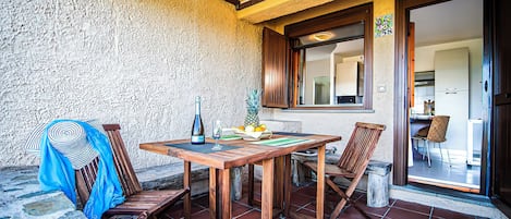 Uma mesa de madeira com cadeiras, uma garrafa e um copo no pátio.