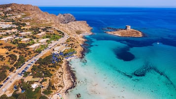 An aerial view of a coastal area with a beach, a rocky outcrop, and a tower.