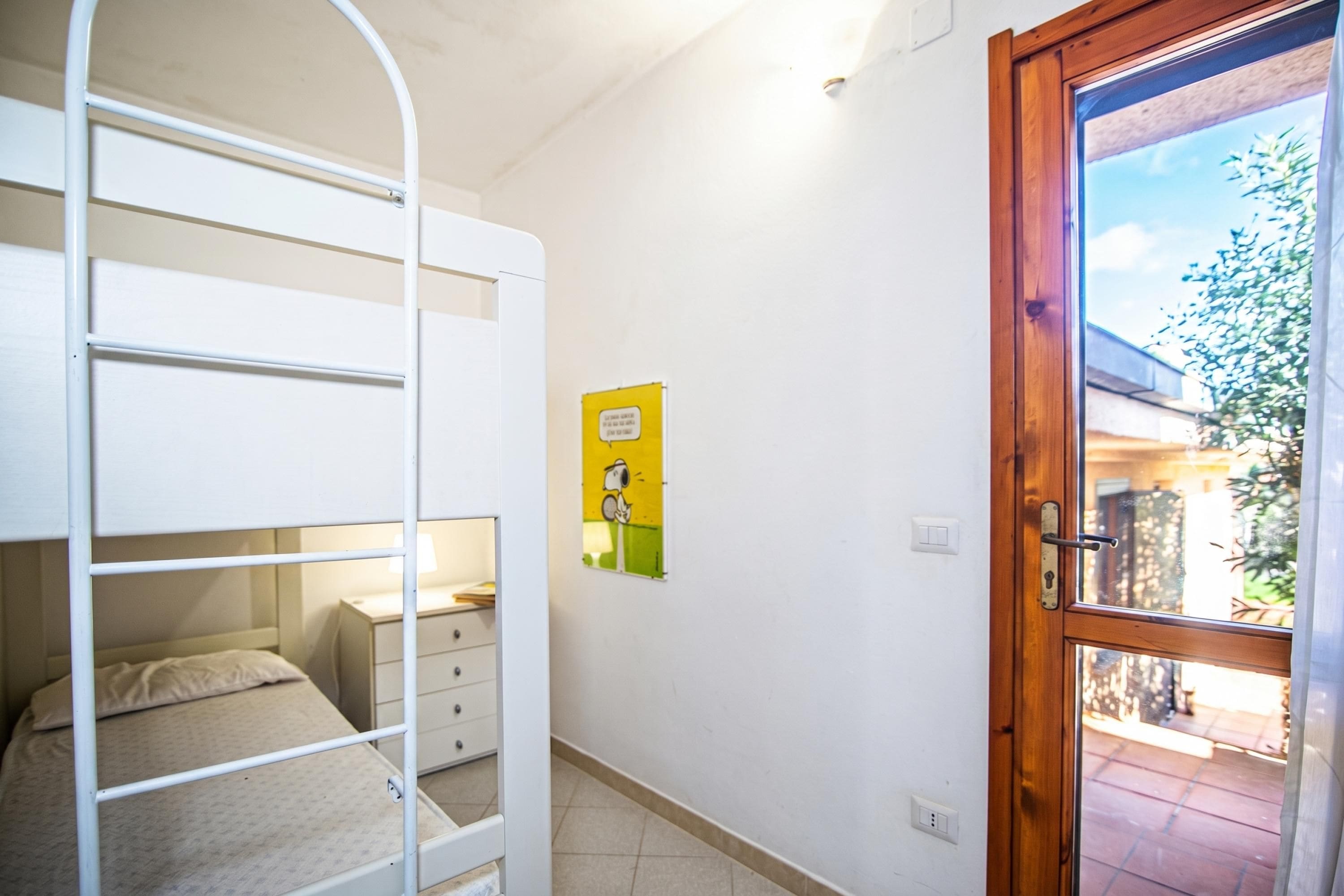 Una cama litera con un escritorio pequeño, una puerta de madera y una ventana que da a un paisaje exterior.