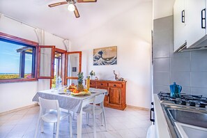 A kitchen with a dining table, chairs, a stove, a cabinet, and a window with a view. - 1 Le Perle Di Stintino (Stintino)