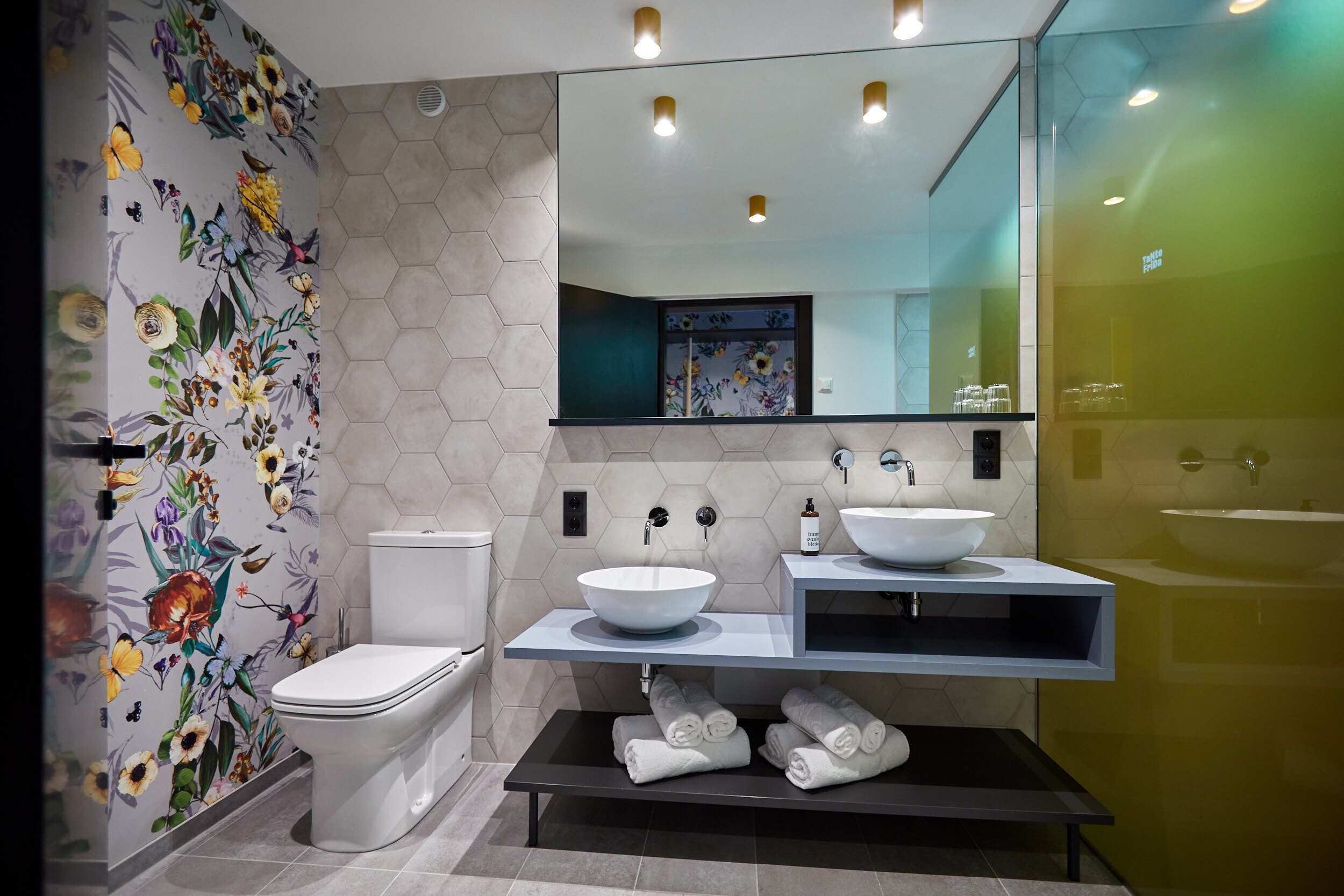 Un baño moderno con inodoro, dos lavamanos, un espejo grande y un perchero para toallas.