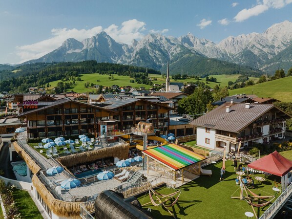 A hotel with multiple buildings, a pool area with umbrellas, and a view of mountains. - EdeR FriDa – Family Hotel – Tuttiii KomPletti ALL InKlusiv (Maria Alm am Steinernen Meer)