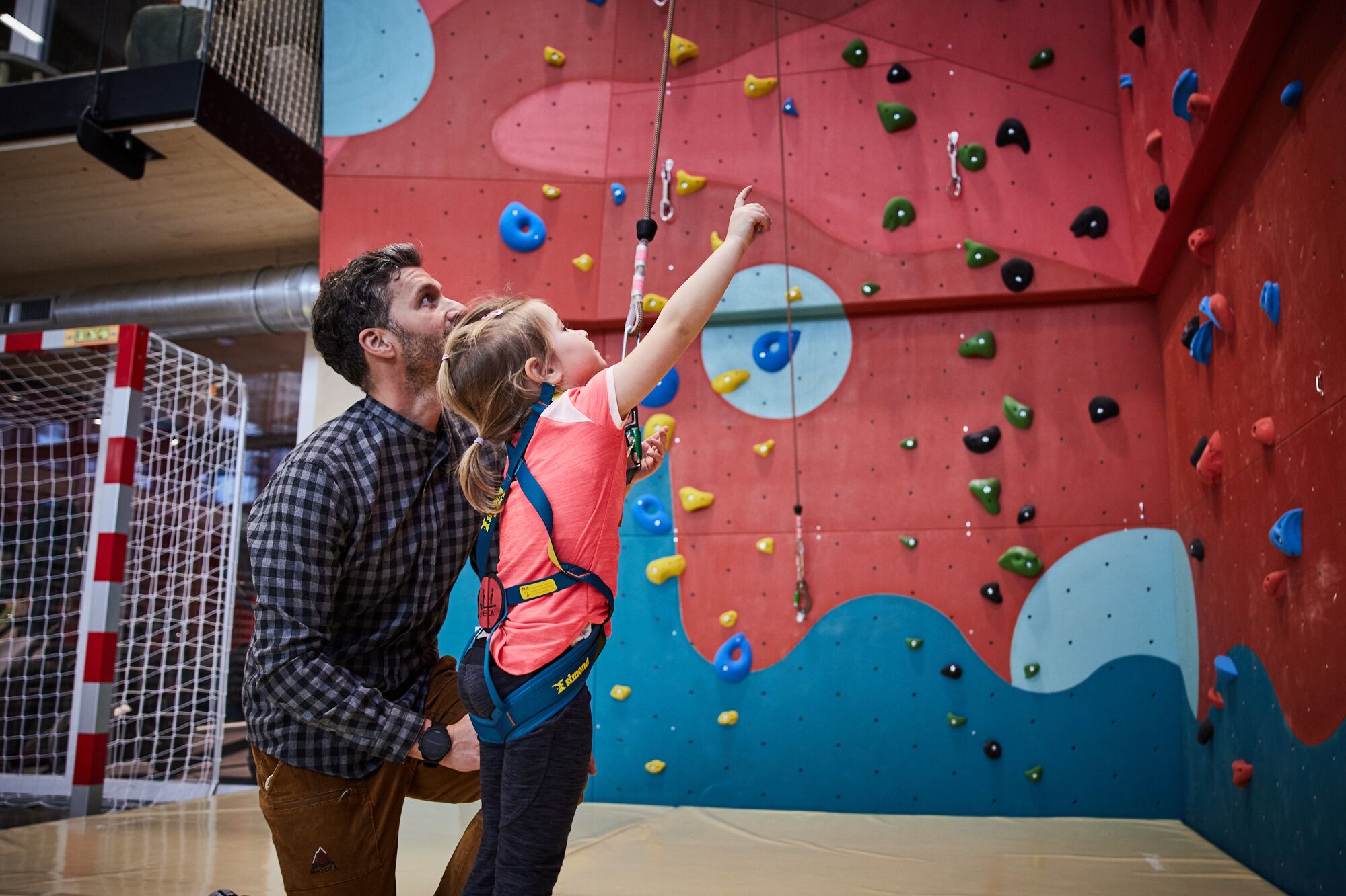 Eine Person klettert an einer bunten Indoor-Kletterwand mit unterschiedlichen Haltepunkten.