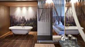 Un baño moderno con dos tinas separadas, un espejo grande y un mural de un paisaje boscoso.