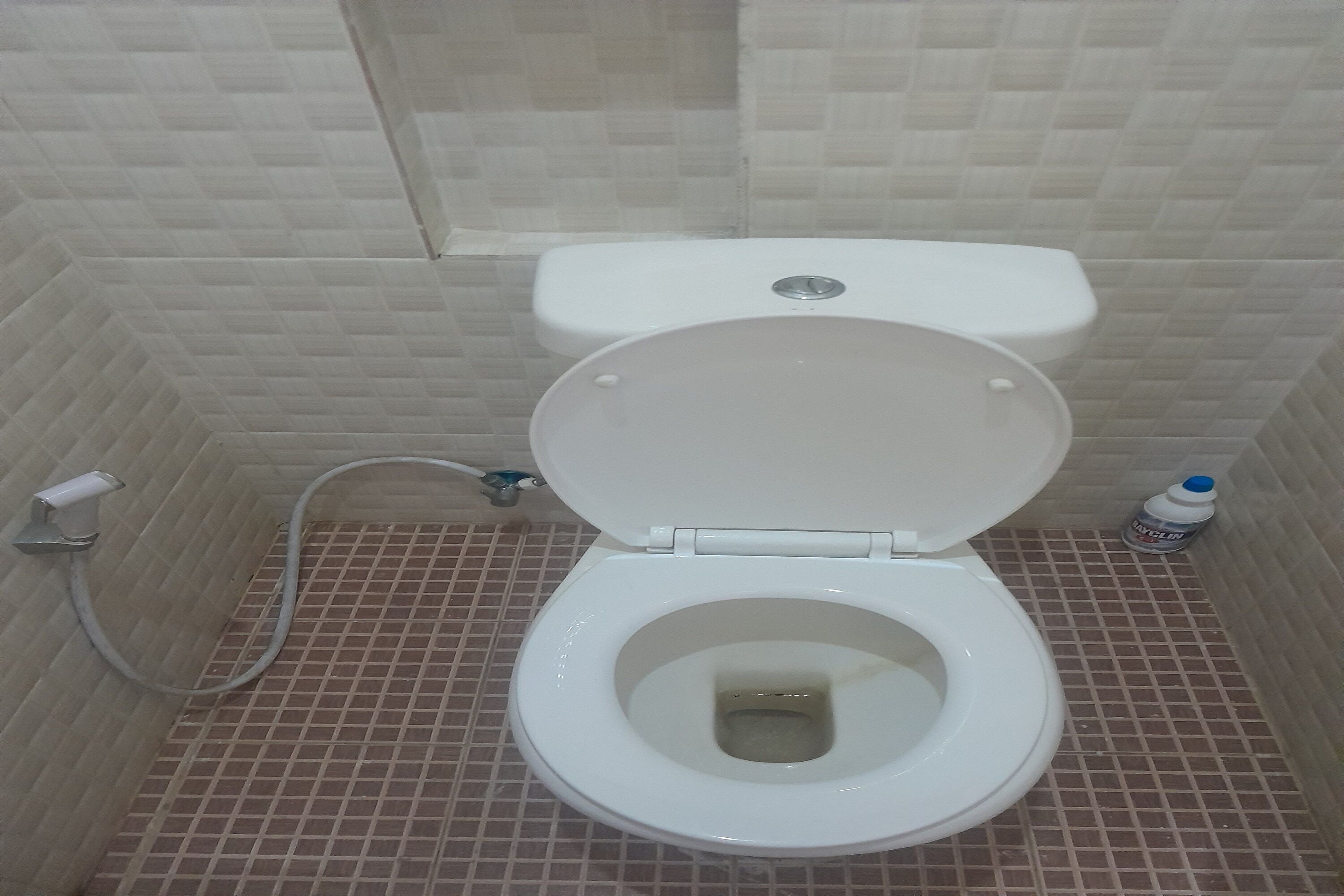 Un baño con inodoro blanco, ducha y suelo de baldosas.