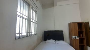 A single bed with a headboard, a window with bars, and a wooden bookshelf.