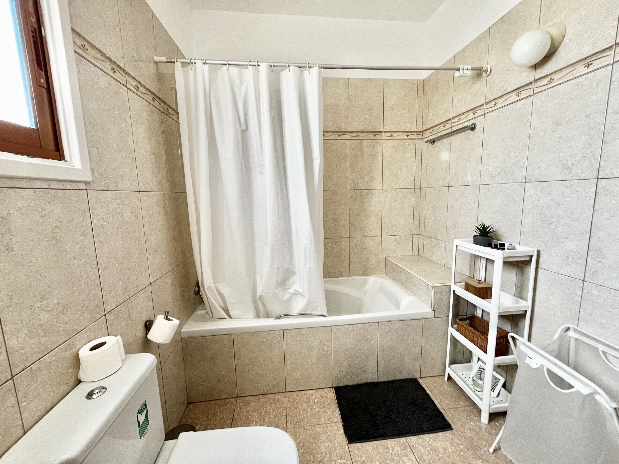 A bathroom with a bathtub, toilet, and shelves with toiletries.