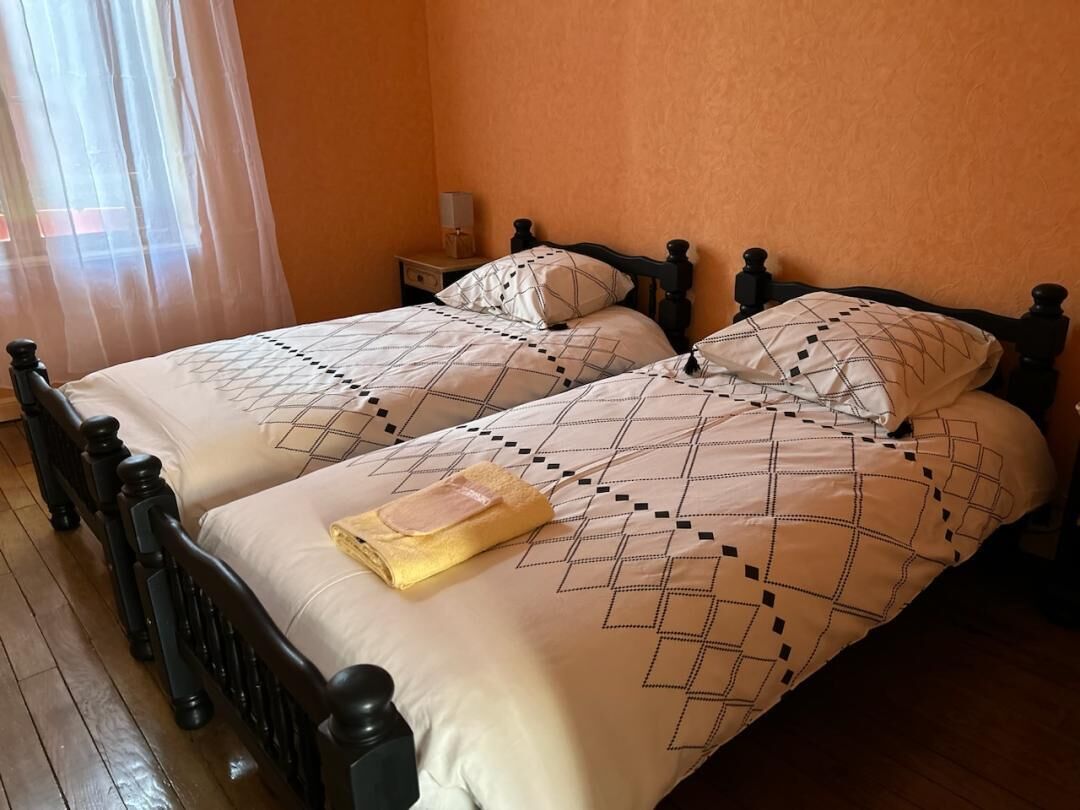 Una habitación con dos camas, cada una con un edredón y almohadas estampadas, piso de madera y una mesita de noche con lámpara.