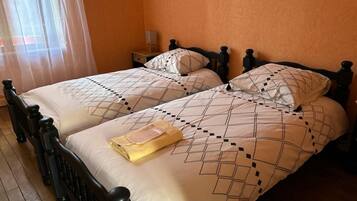 Una habitación con dos camas, cada una con un edredón y almohadas estampadas, piso de madera y una mesita de noche con lámpara.