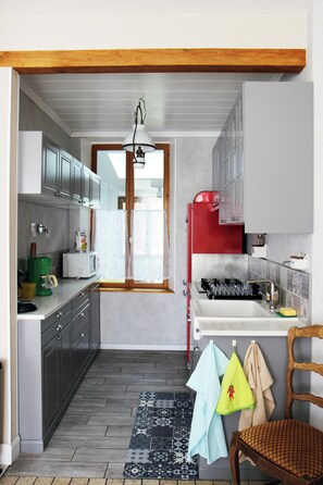 A compact kitchen with grey cabinets, a red appliance, a sink, and a chair.