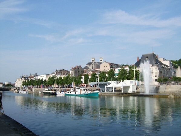 A waterfront view with boats, a fountain, and buildings in the background.
