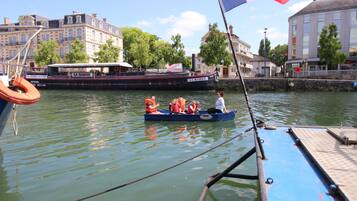 Ein Boot mit Passagieren in Rettungswesten, vertäut neben einem Gebäude mit der Aufschrift 'LA BARGE'.
