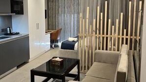 A modern living room with a sofa, a coffee table, and a TV. There is a kitchen area with a microwave and a coffee machine. - Luxsugero Studios (Noida)