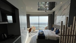 A modern bedroom with a large bed, a desk, and a view of the city. - Luxsugero Studios (Noida)