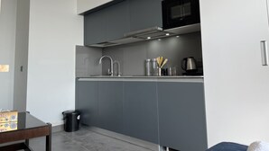 A modern kitchen with grey cabinets, a stainless steel sink, a microwave, and a kettle. - Luxsugero Studios (Noida)