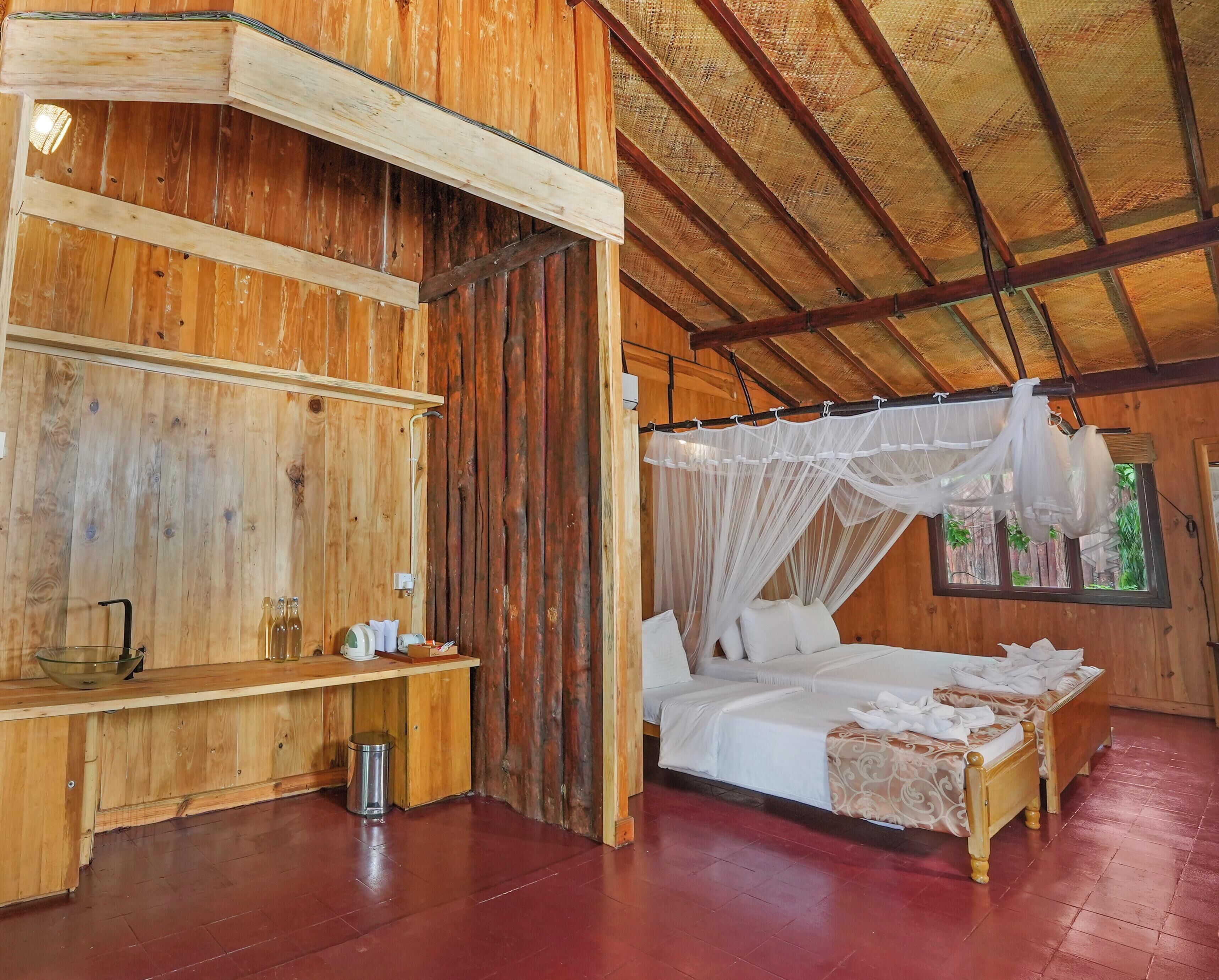 A wooden room with a bed, a bedside table, and a window with a view of greenery.