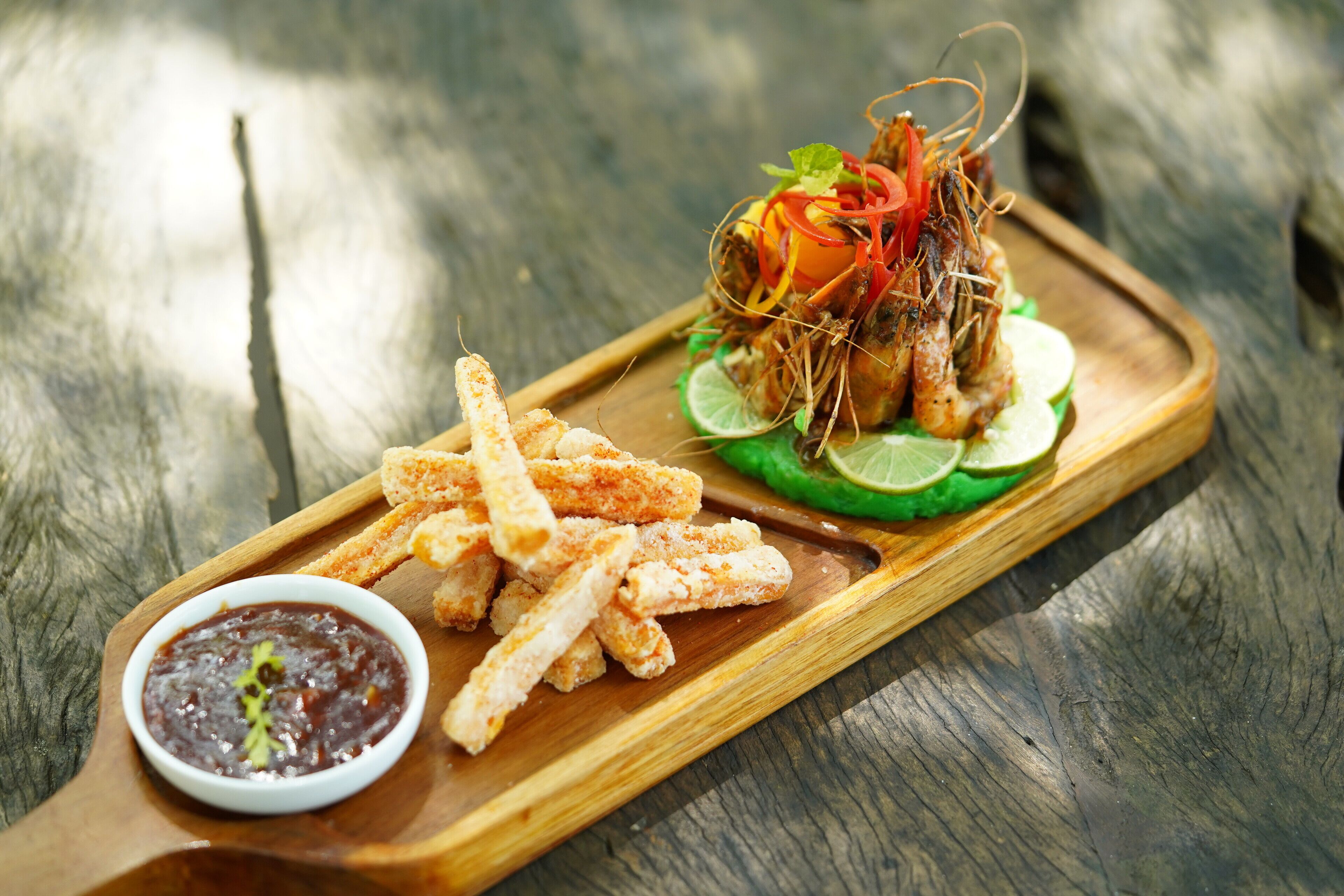 A wooden serving tray with fried shrimp, lemon slices, and a small bowl of sauce.