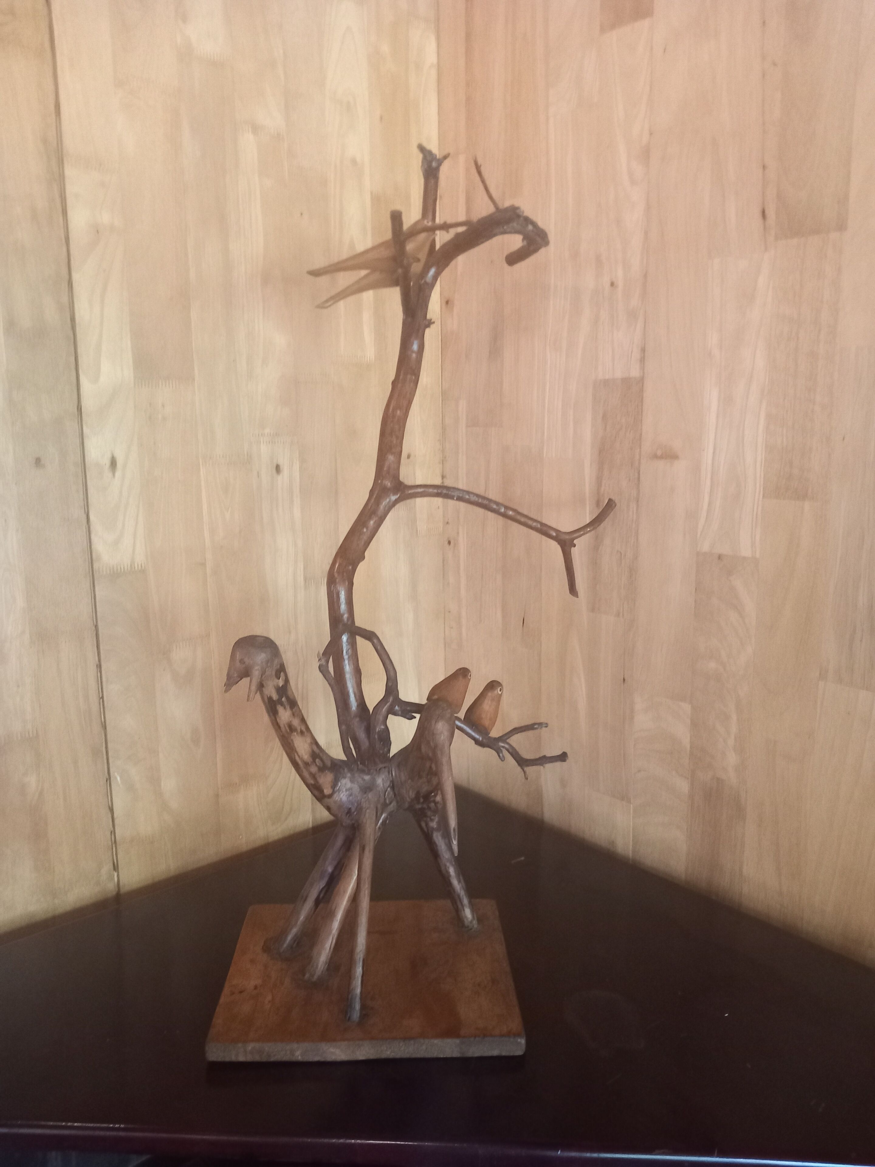 Une sculpture métallique représentant un arbre avec des branches et des feuilles, montée sur un socle en bois.