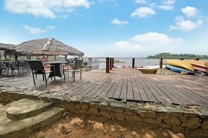 Una terraza de madera con una estructura de techo de paja, una mesa con sillas y vista al agua.