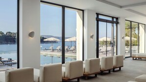 A modern hotel lobby with large windows offering a view of a pool and lounge area. - The Isolano, Cres, Autograph Collection (Cres)
