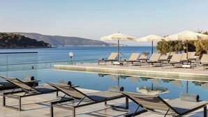 A poolside area with lounge chairs and umbrellas, overlooking a body of water and distant hills. - The Isolano, Cres, Autograph Collection (Cres)
