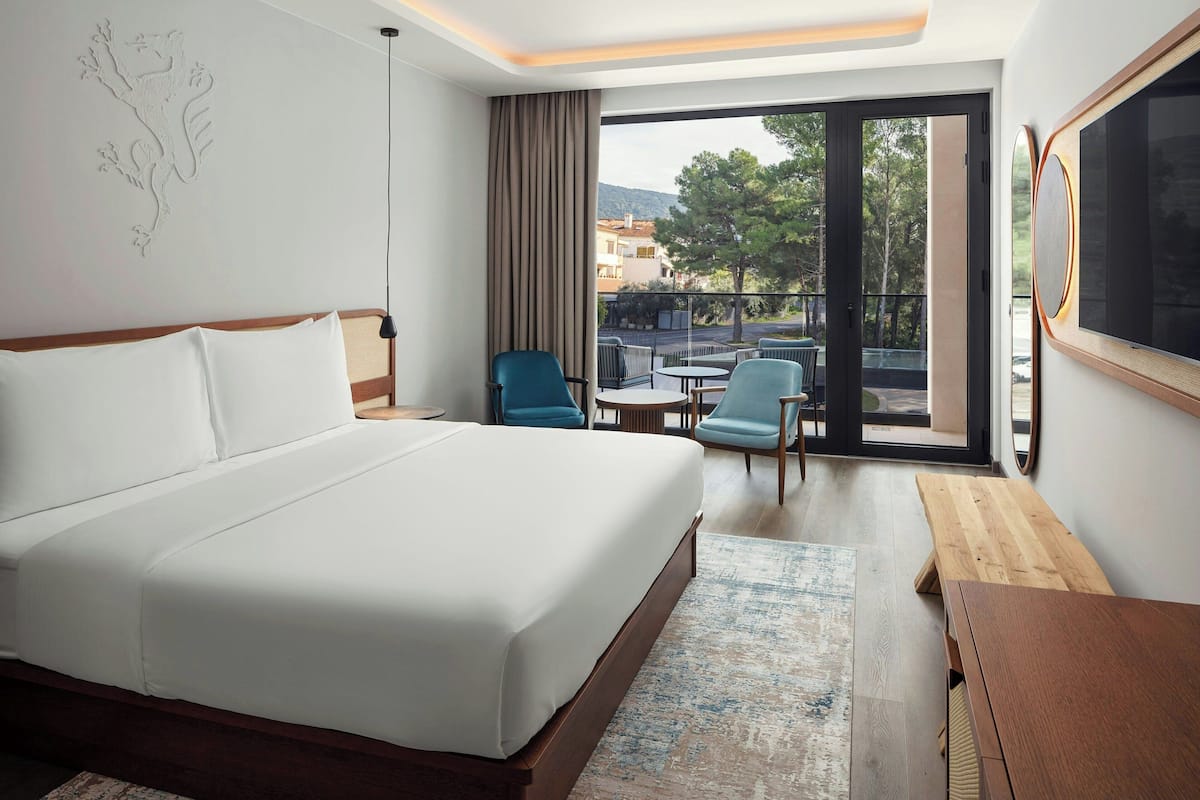 Une chambre d’hôtel dotée d’un grand lit, d’un coin salon avec des fauteuils et une table, et d’un balcon offrant une vue sur la ville.