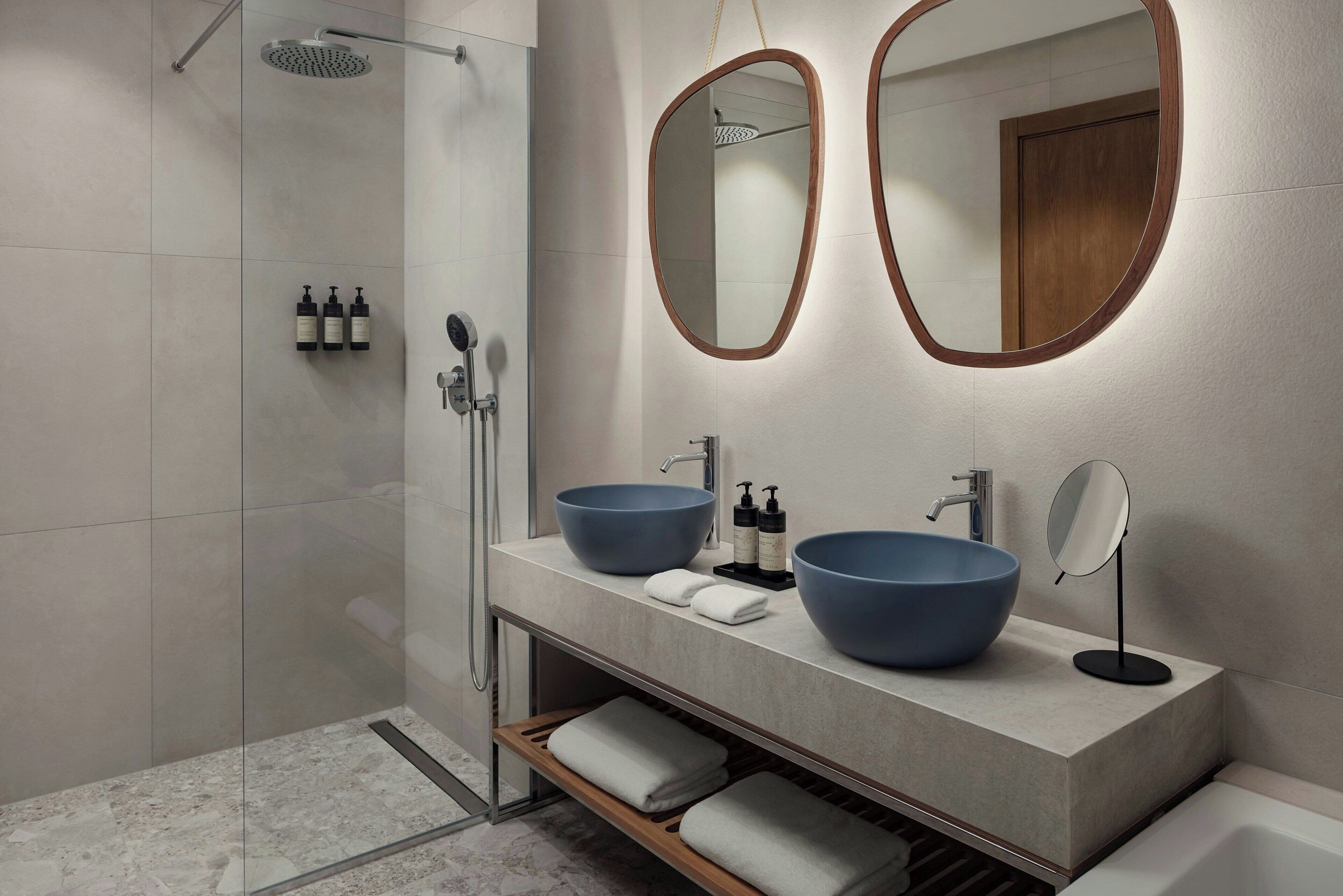 A modern bathroom with two large blue sinks, a shower, and two mirrors with wooden frames.